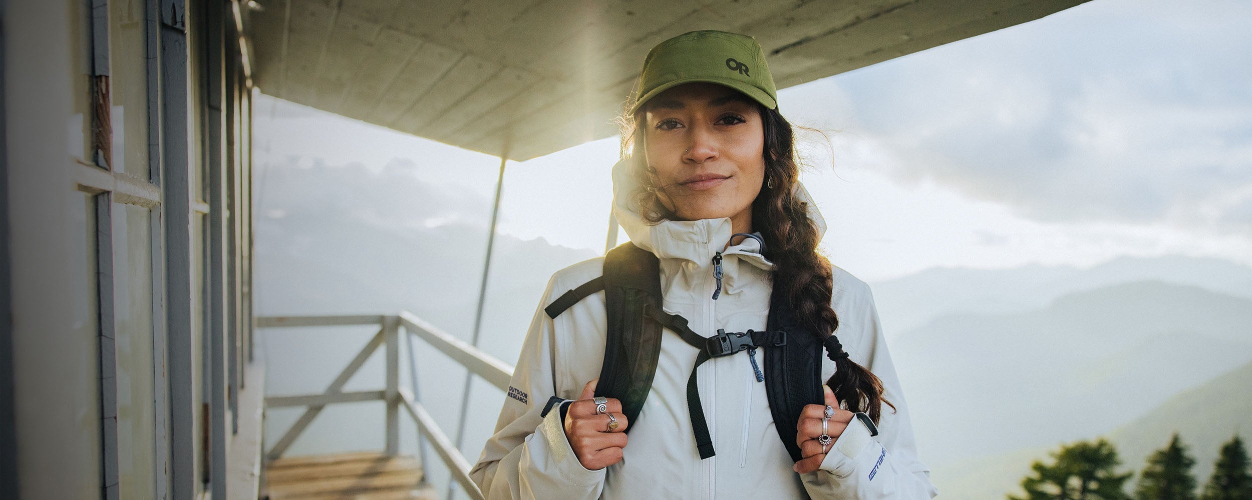 Sun shines on a woman while she smiles wearing Outdoor Research Aspire 3L Jacket in Oyster/White.