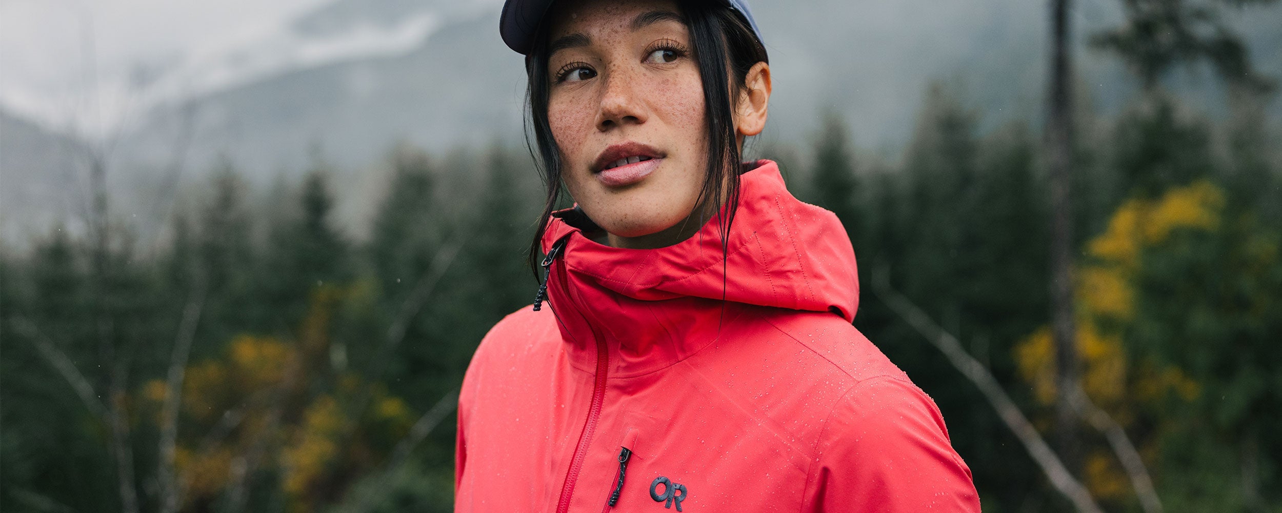 Woman looks and admires the nature and trees around her while wearing the Outdoor Research Aspire 3L Jacket.