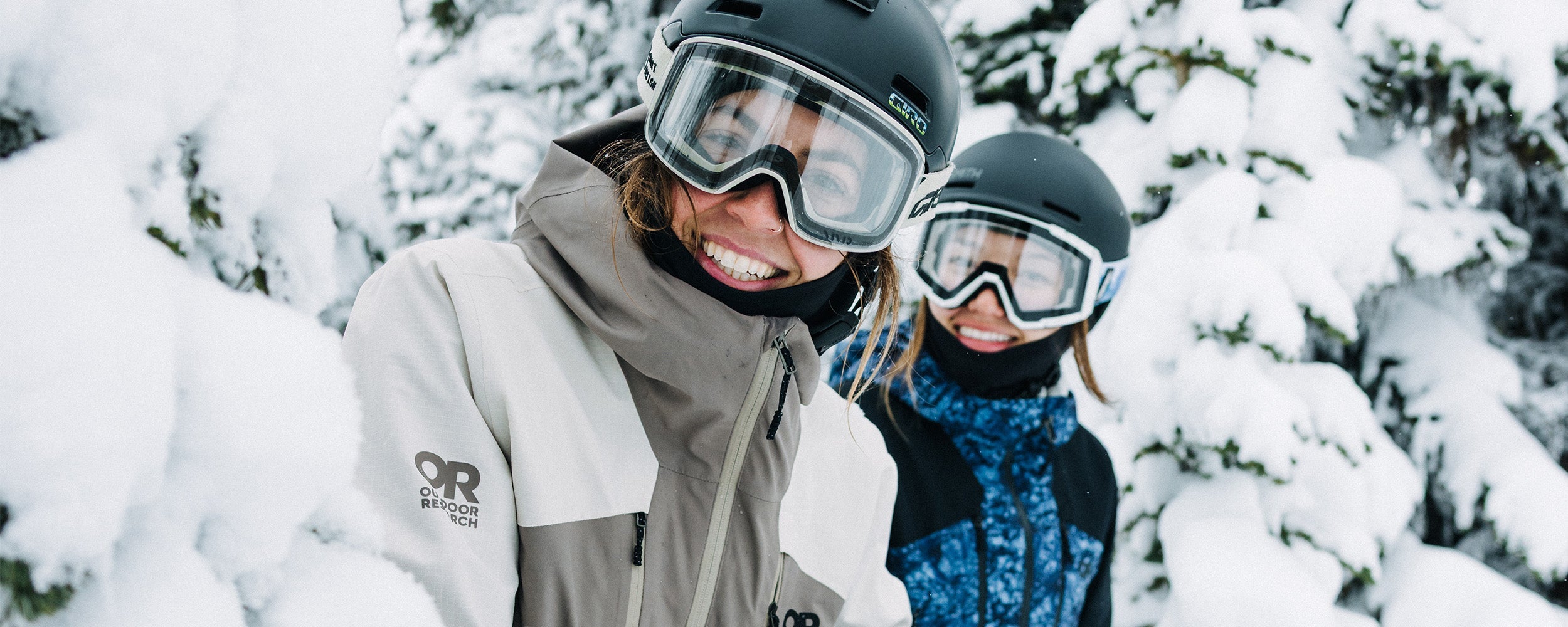 2 friends in the thick snow wearing Outdoor Research Women's Powderverse Jacket Oyster/Sable and Summit Granite Print/Black. 