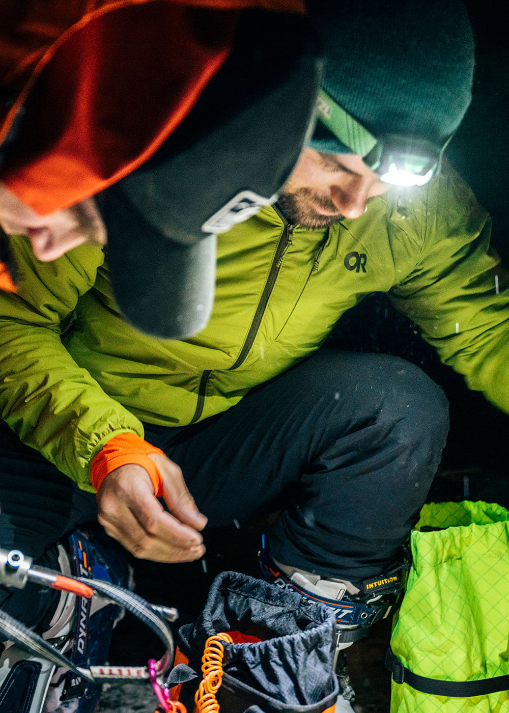 Two friends in the dark with flashlights looking down wearing Outdoor Research Men's Vesper Insulated Hoodie Rainforest Green. 