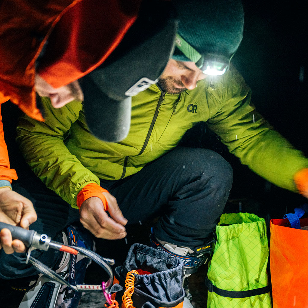 Two friends in the dark with flashlights looking down wearing Outdoor Research Men's Vesper Insulated Hoodie Rainforest Green. 